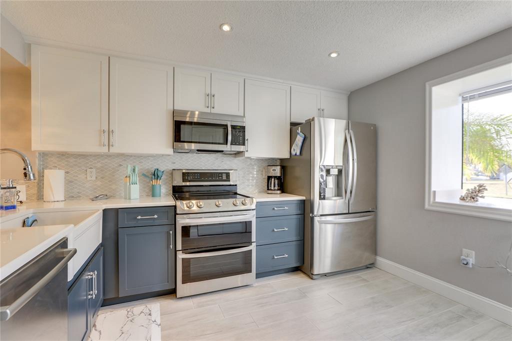 A kitchen features white upper cabinets, dark blue lower cabinets, stainless steel appliances, and tile flooring — 6010 36TH AVENUE CIRCLE W, BRADENTON, FL