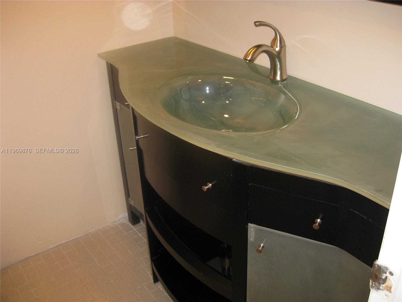 A bathroom vanity features a frosted glass countertop, a curved basin, and dark cabinetry — 3181 S Ocean Dr # 304, Hallandale Beach FL 33009, HALLANDALE BEACH, FL
