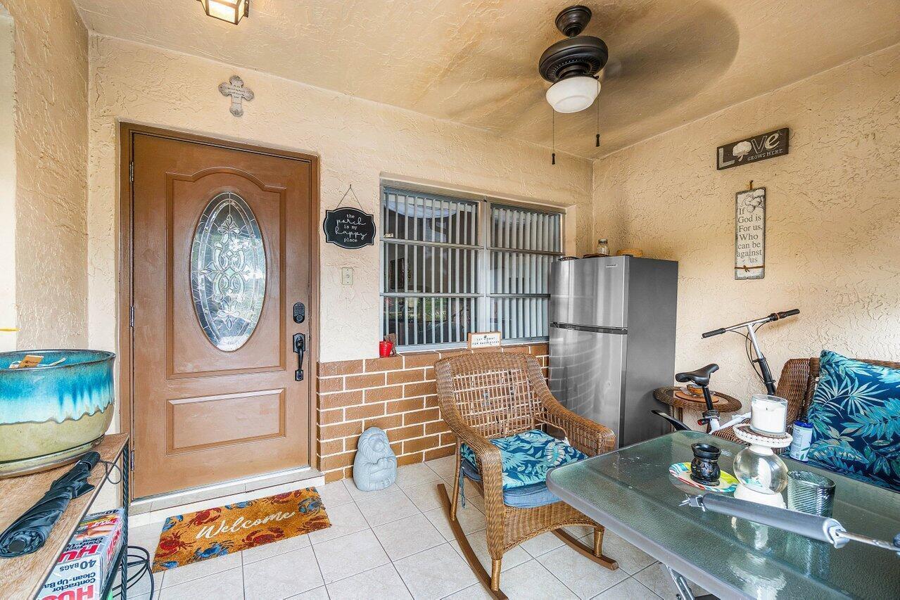 A covered porch features a front door, a wicker chair, a refrigerator, and a table — 5814 Doris Court, Delray Beach FL 33484, DELRAY BEACH, FL