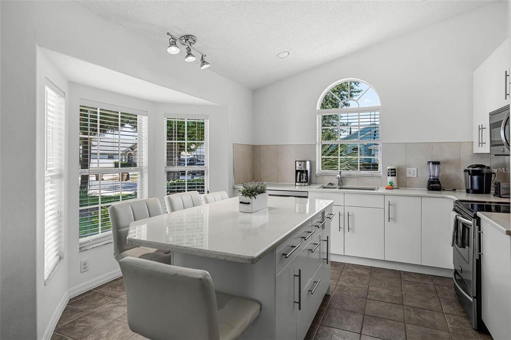 A kitchen features a white island, light countertops, white cabinetry, and a dining nook — 8065 INDIAN CREEK BOULEVARD, KISSIMMEE, FL