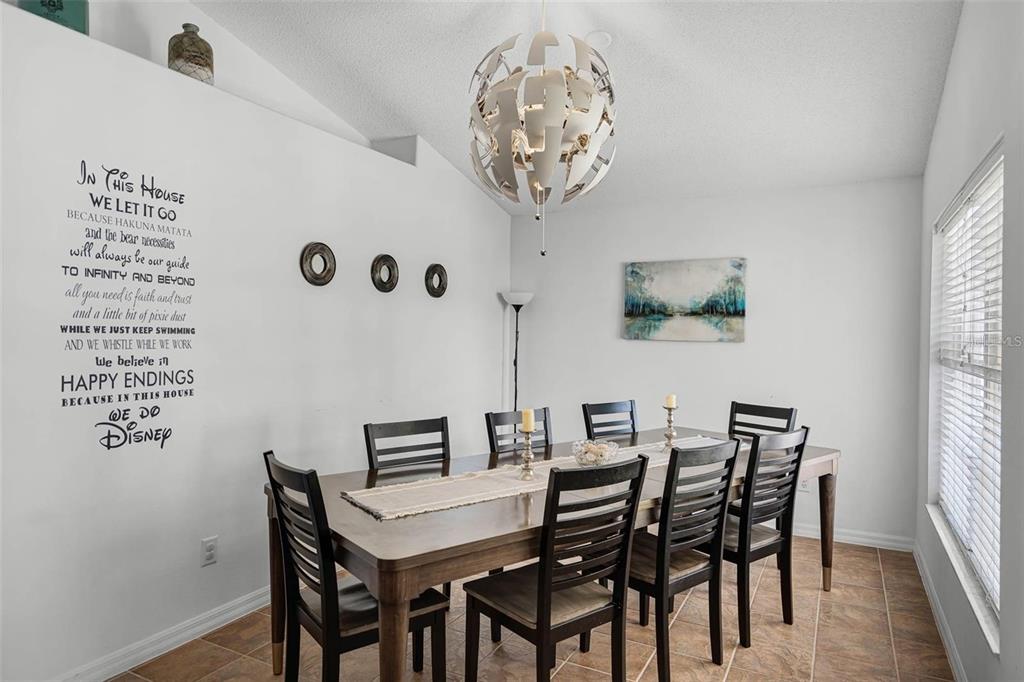 A dining room features a wooden table with six chairs, a modern chandelier, and wall decals — 8065 INDIAN CREEK BOULEVARD, KISSIMMEE, FL