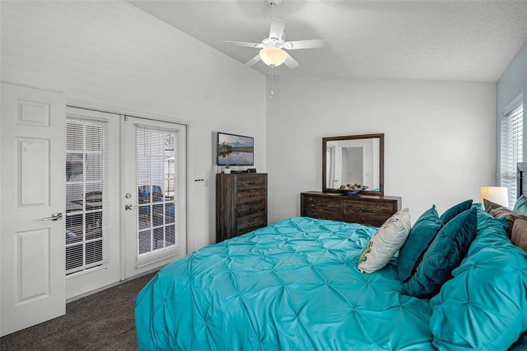 A bedroom features a turquoise tufted bedspread, dark wood furniture, and glass-paned French doors — 8065 INDIAN CREEK BOULEVARD, KISSIMMEE, FL