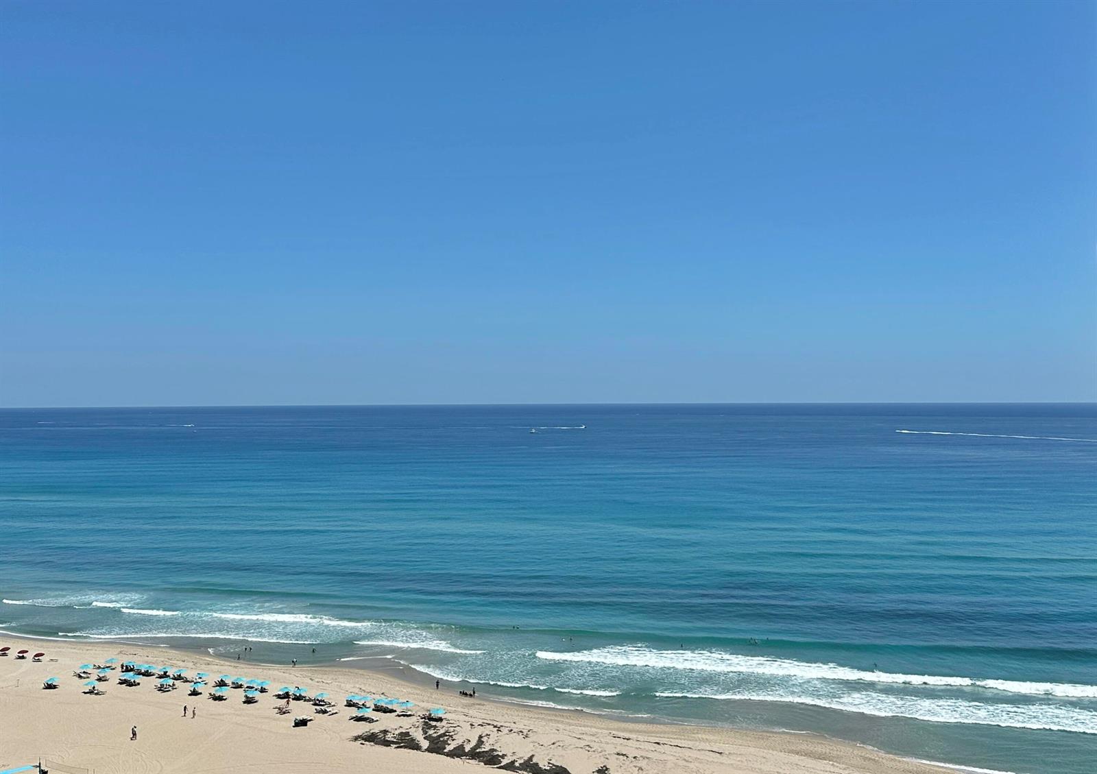 A high-angle view of a sandy beach with blue umbrellas and the ocean beyond — 3000 N Ocean Drive # b, Singer Island FL 33404, SINGER ISLAND, FL