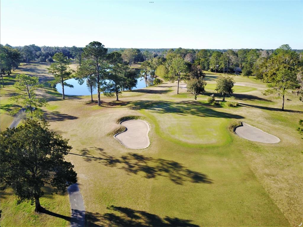 An aerial view of a golf course hole featuring sand bunkers, green grass, and a pond — NW 109TH PLACE, ALACHUA, FL