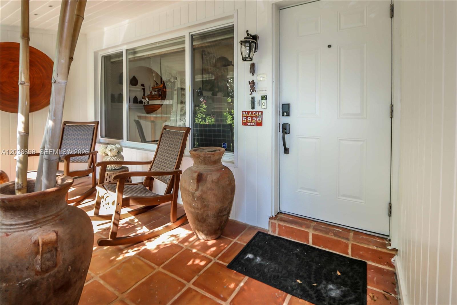 A covered porch features terracotta tile flooring, two rocking chairs, and a white front door — 1251 Buchanan St, Hollywood FL 33019, HOLLYWOOD, FL