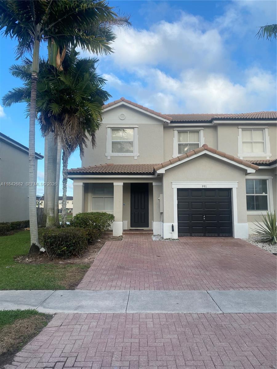 A two-story townhouse features a brick driveway, a black garage door, and a palm tree — 991 NE 42nd Ave # 0, Homestead FL 33033, HOMESTEAD, FL