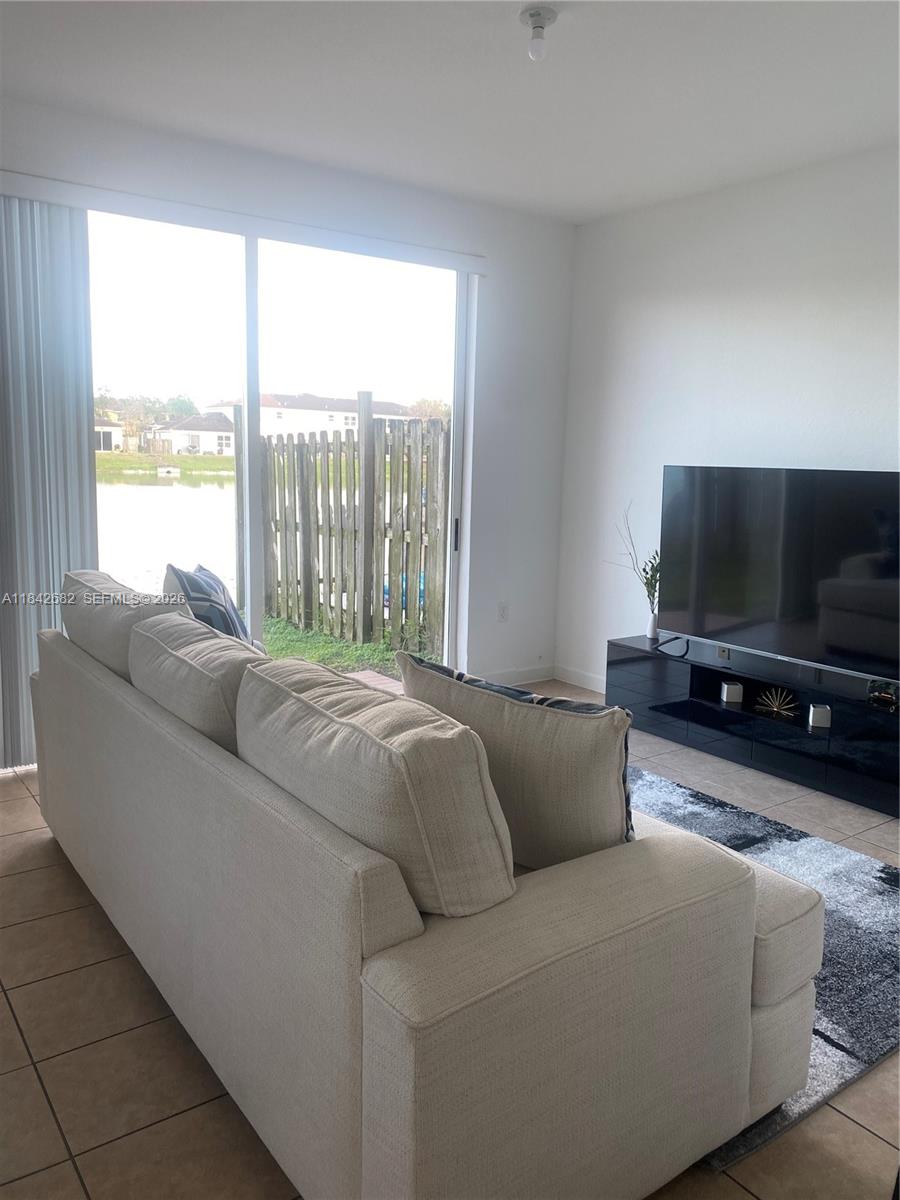 A living room features a beige sofa, a black media console, and sliding glass doors — 991 NE 42nd Ave # 0, Homestead FL 33033, HOMESTEAD, FL