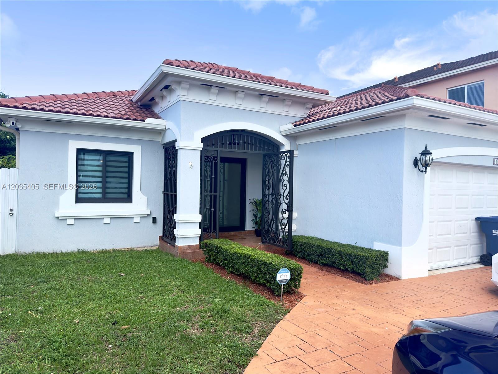 A light blue single-story house features a tiled roof, arched entryway, and a paved driveway — 17833 SW 155th Ct, Miami FL 33187, MIAMI, FL