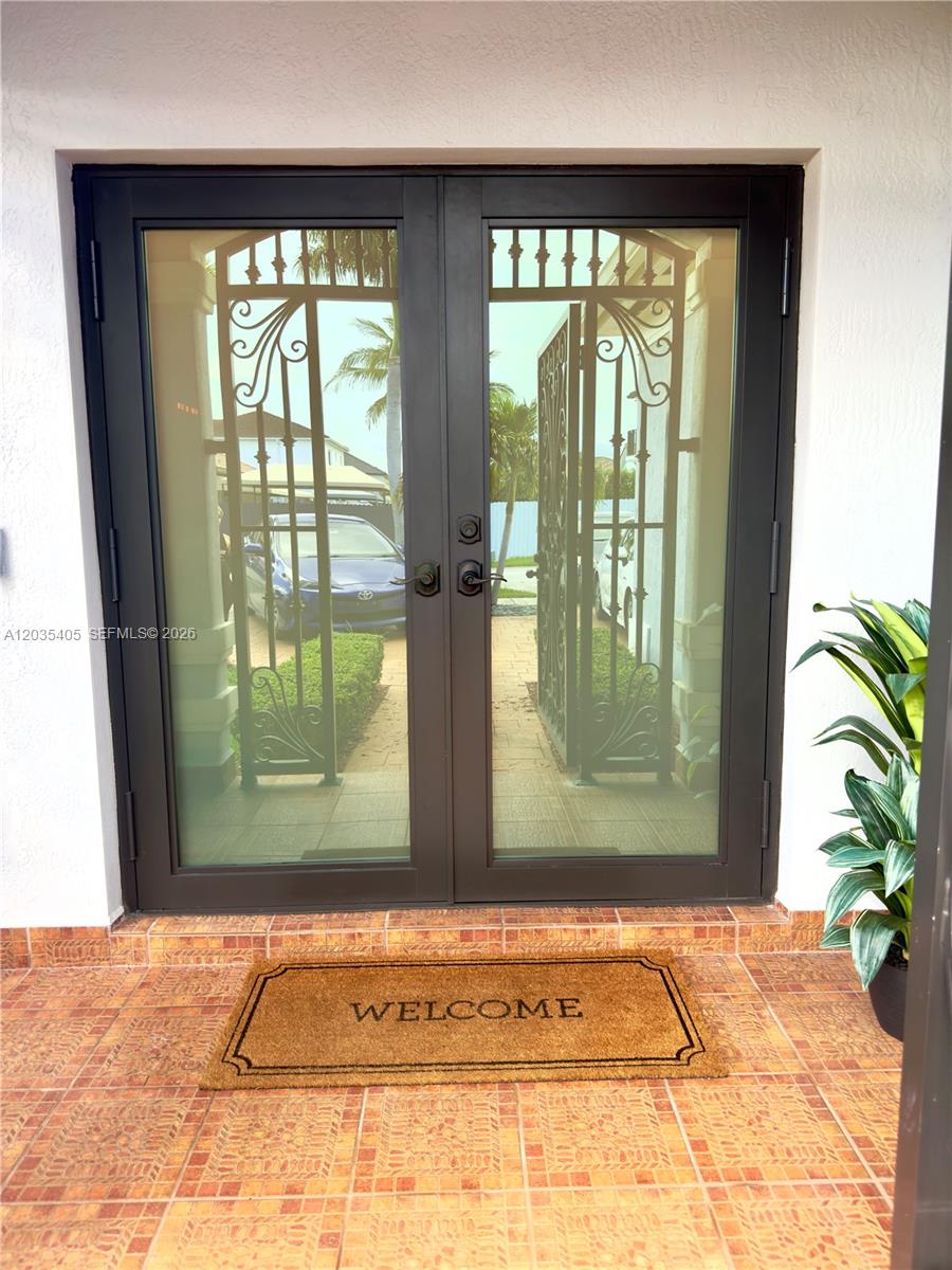 A pair of dark-framed glass double doors with decorative metal grilles opens onto a tiled porch — 17833 SW 155th Ct, Miami FL 33187, MIAMI, FL
