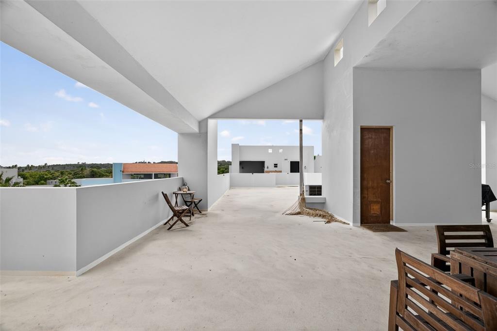 A spacious, open-air concrete rooftop terrace features a partial roof, white walls, and outdoor furniture — Paraíso del Atlántico CARR. 4485 Apt. 307, QUEBRADILLAS, PR