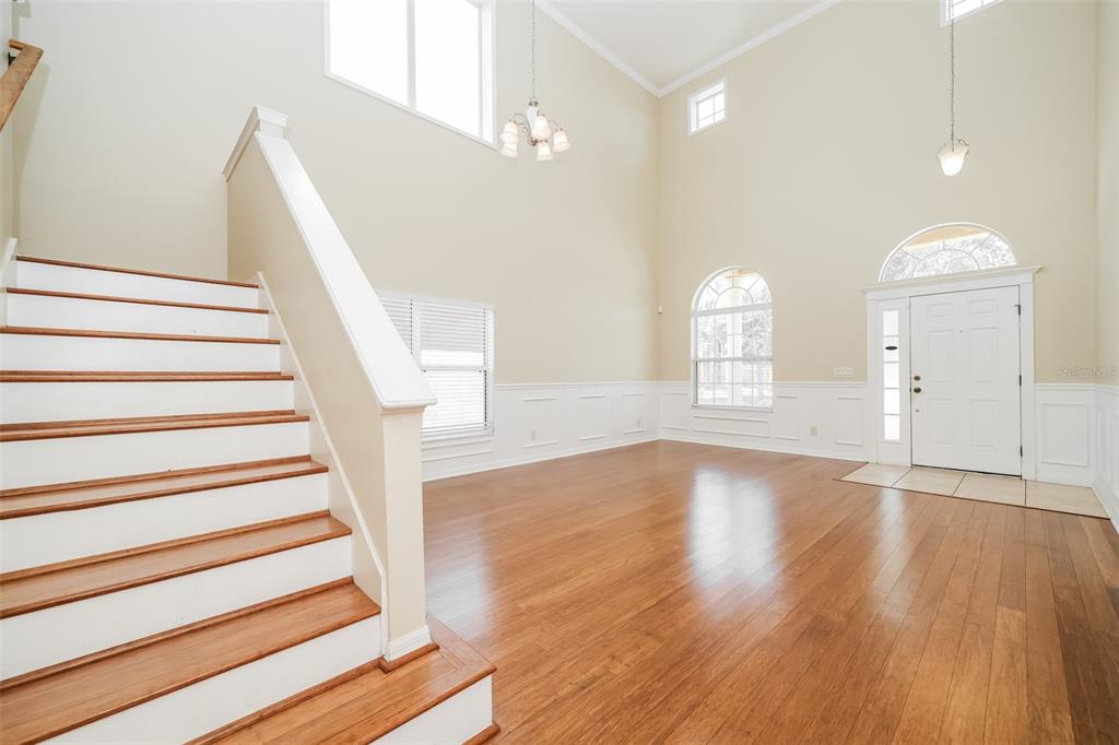 A bright foyer features hardwood floors, a high ceiling, and a staircase with white railings — 7318 FOREST MERE DRIVE, RIVERVIEW, FL