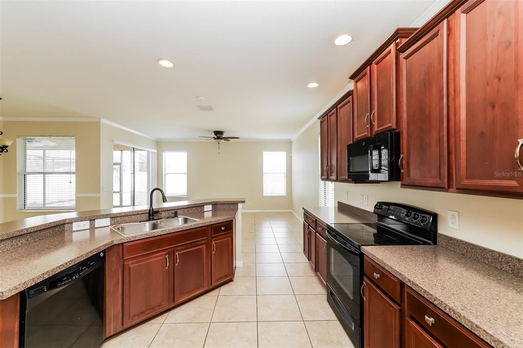 A kitchen with wood cabinets, black appliances, and tan countertops features a tile floor — 7318 FOREST MERE DRIVE, RIVERVIEW, FL