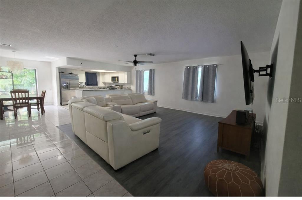 An open-concept living room features white leather sofas, dark wood-look flooring, and a kitchen beyond — 47 & 49 SANDPIPER CIRCLE UNIT 47 & 49, ORMOND BEACH, FL