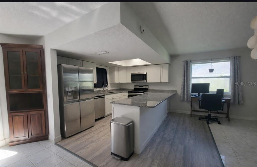 A kitchen with white cabinets, granite countertops, stainless steel appliances, and a wood-look floor — 47 & 49 SANDPIPER CIRCLE UNIT 47 & 49, ORMOND BEACH, FL