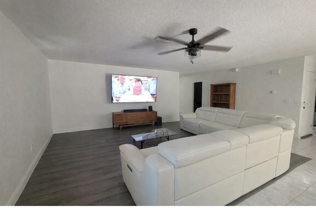 A living room features a white sectional sofa, a wall-mounted television, and wood-look flooring — 47 & 49 SANDPIPER CIRCLE UNIT 47 & 49, ORMOND BEACH, FL
