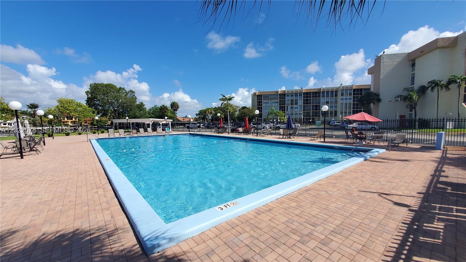 A rectangular outdoor swimming pool is surrounded by a brick patio and lounge chairs — 801 Three Islands Blvd # 109, Hallandale Beach FL 33009, HALLANDALE BEACH, FL