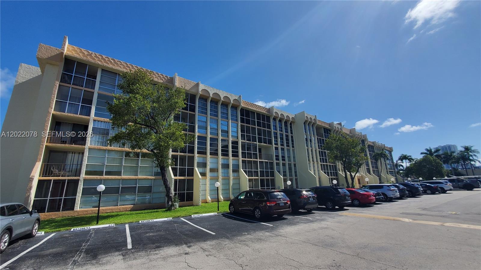 A multi-story apartment building with a parking lot in the foreground under a blue sky — 801 Three Islands Blvd # 109, Hallandale Beach FL 33009, HALLANDALE BEACH, FL