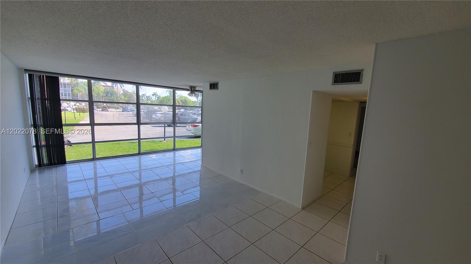 A bright, empty room features white tile floors, large floor-to-ceiling windows, and a doorway — 801 Three Islands Blvd # 109, Hallandale Beach FL 33009, HALLANDALE BEACH, FL