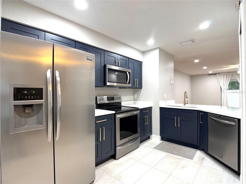 A kitchen features dark blue cabinets, stainless steel appliances, white countertops, and light tile flooring — 4815 WALDEN CIRCLE UNIT 75, ORLANDO, FL