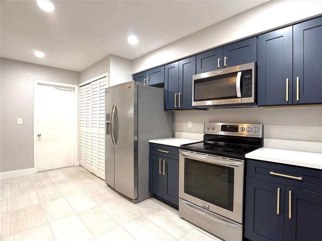 A kitchen features dark blue cabinets, stainless steel appliances, and light-colored tile flooring — 4815 WALDEN CIRCLE UNIT 75, ORLANDO, FL