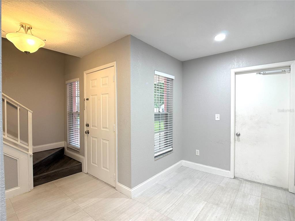 An entryway features light tile flooring, gray walls, a staircase, and two white doors — 4815 WALDEN CIRCLE UNIT 75, ORLANDO, FL