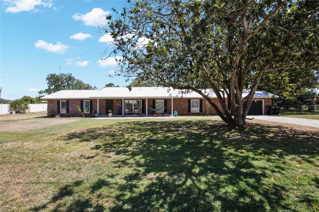A single-story brick house with a white metal roof sits behind a large shade tree — 317 NW 7TH STREET, WILLISTON, FL