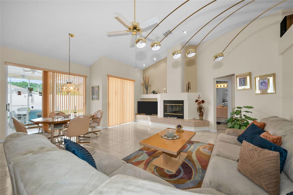 A living room features a fireplace, tile flooring, a ceiling fan, and an arched floor lamp — 7405 EVESBOROUGH LANE, NEW PORT RICHEY, FL