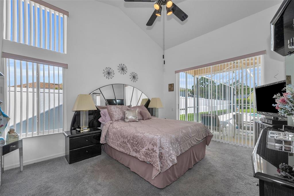 A bedroom features a bed with a mirrored headboard, vaulted ceilings, and large sliding glass doors — 7405 EVESBOROUGH LANE, NEW PORT RICHEY, FL