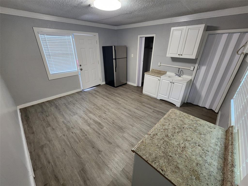 A small kitchen area features gray walls, wood-look flooring, white cabinets, and a stainless refrigerator — 407 S JUPITER AVENUE UNIT 7, CLEARWATER, FL