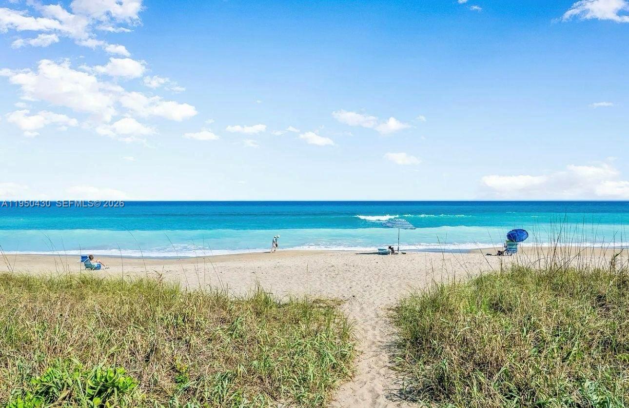 A sandy path leads through beach grass to the ocean with umbrellas and people — 10044 S Ocean dr # 105, Jensen Beach FL 34957, JENSEN BEACH, FL