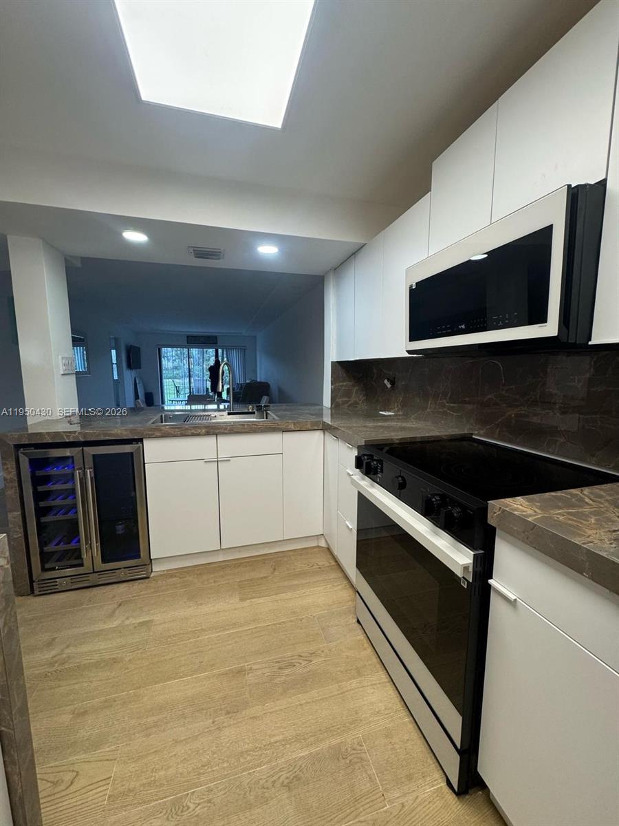 A kitchen features white cabinets, dark stone countertops, a wine cooler, and light wood flooring — 10044 S Ocean dr # 105, Jensen Beach FL 34957, JENSEN BEACH, FL