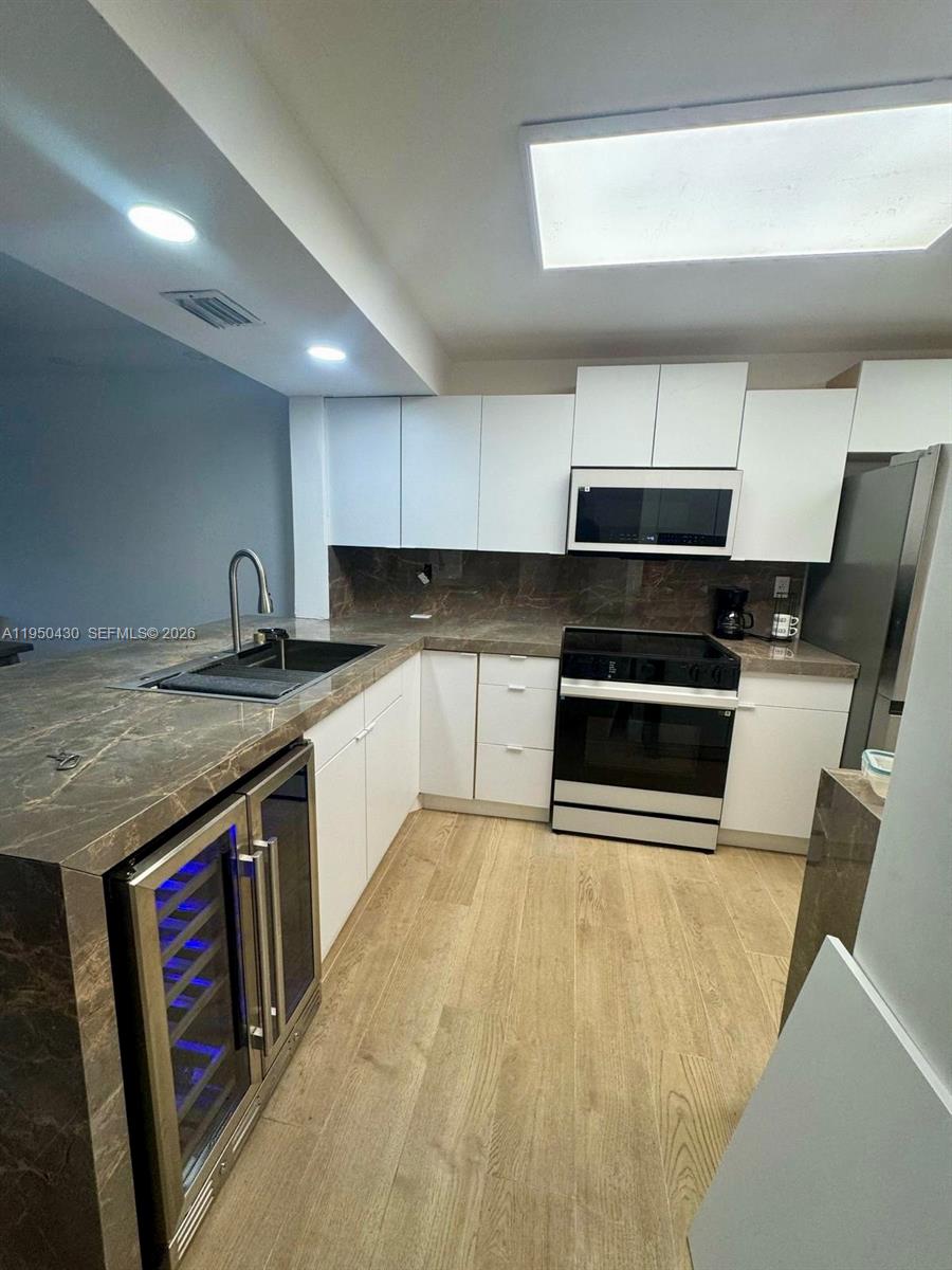 A modern kitchen features white cabinets, dark marble countertops, and light wood-look flooring — 10044 S Ocean dr # 105, Jensen Beach FL 34957, JENSEN BEACH, FL