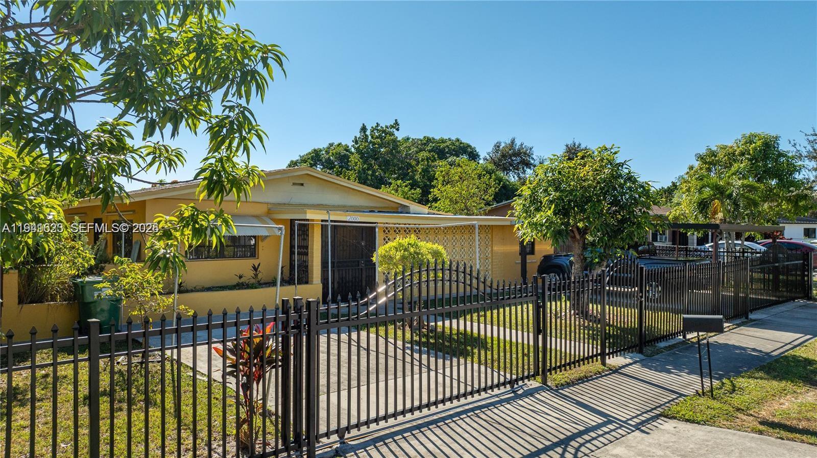 A yellow single-story house features a black metal fence and a gated driveway — 2000 NW 131st St, Miami FL 33167, MIAMI, FL