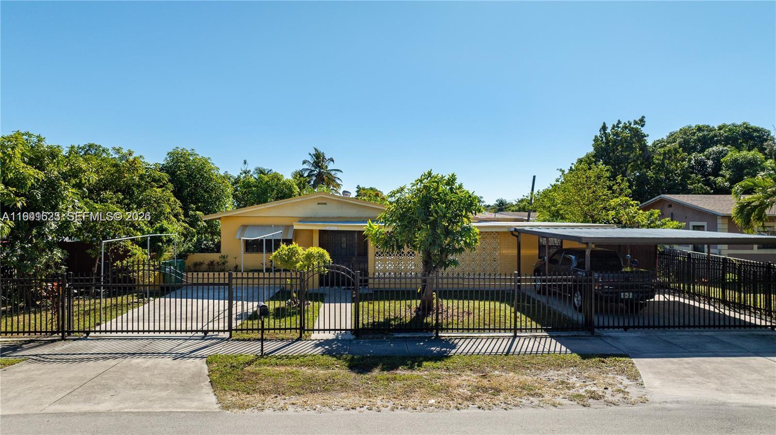 A yellow single-story house features a metal fence, a carport, and a paved driveway — 2000 NW 131st St, Miami FL 33167, MIAMI, FL