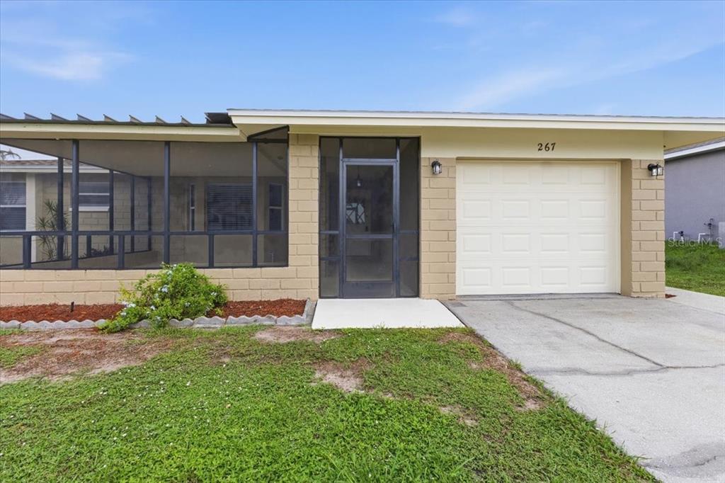A single-story house features a tan block exterior, a screened-in porch, and a white garage — 267 ANNAPOLIS LANE, ROTONDA WEST, FL