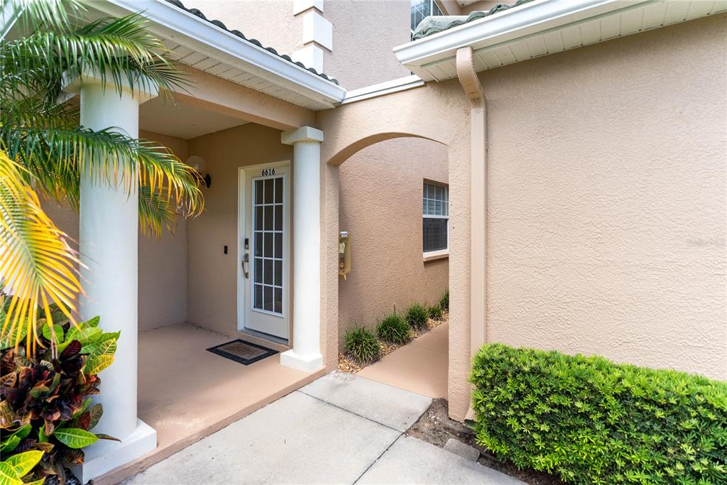 The exterior view shows a covered entryway with a white door, columns, and landscaping — 6616 7TH AVENUE CIRCLE W UNIT 1311, BRADENTON, FL
