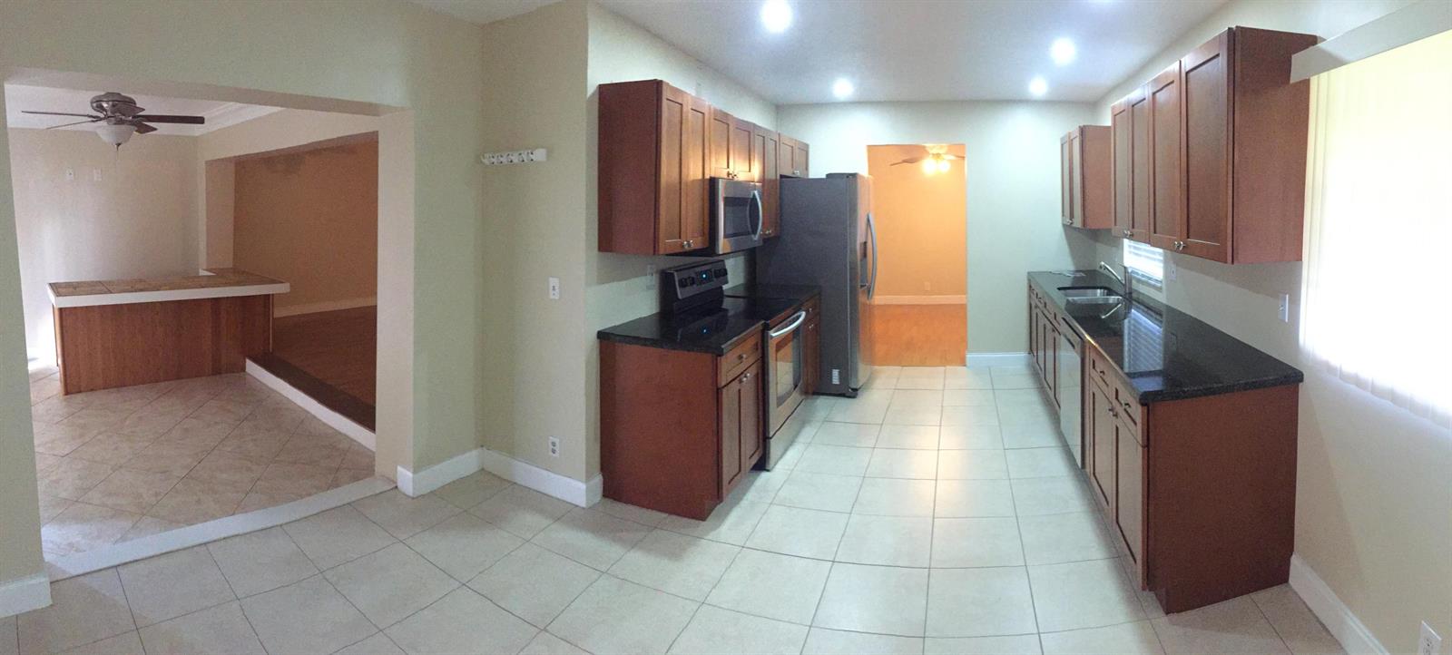 A kitchen with wood cabinets, black countertops, and tile flooring, opening into an adjacent room — 22447 SW 56th Avenue, Boca Raton FL 33433, BOCA RATON, FL