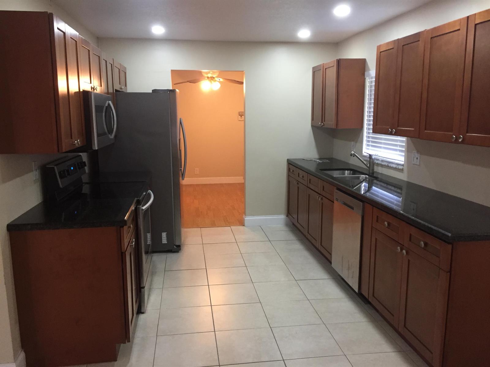 A galley kitchen features wood cabinets, dark countertops, stainless steel appliances, and light tile flooring — 22447 SW 56th Avenue, Boca Raton FL 33433, BOCA RATON, FL