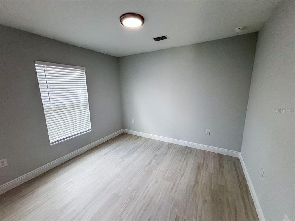 An empty bedroom features light gray walls, wood-look flooring, and a single window with blinds — 9317 AGATE STREET UNIT 9317, PORT CHARLOTTE, FL