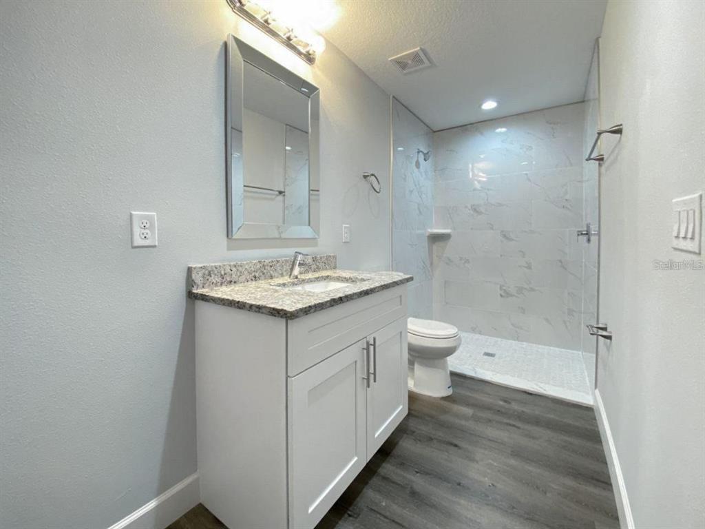 A bathroom features a white vanity with a granite countertop, a mirror, and a walk-in shower — 9317 AGATE STREET UNIT 9317, PORT CHARLOTTE, FL