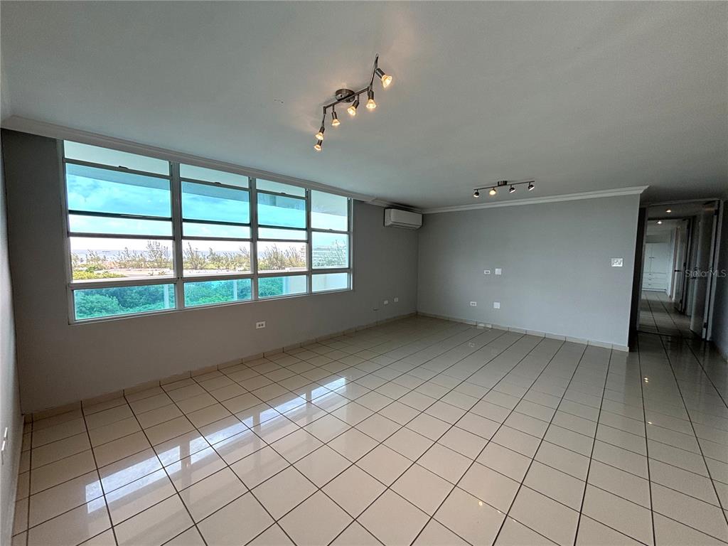 An empty living room features light-colored tile flooring, large windows, and two ceiling-mounted track lights — 550 Avenida Constitucion AVENIDA CONSTITUCION UNIT 901, SAN JUAN, PR