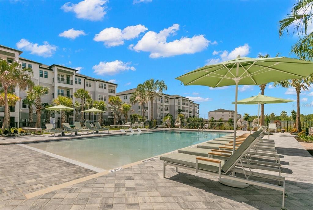 A swimming pool with lounge chairs and umbrellas sits in front of a multi-story apartment building — 1310 RIDGEVIEW CIRCLE UNIT A1, DAVENPORT, FL