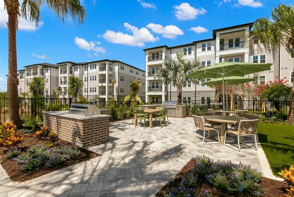 An outdoor patio area features brick grilling stations, dining tables with umbrellas, and apartment buildings — 1310 RIDGEVIEW CIRCLE UNIT A1, DAVENPORT, FL