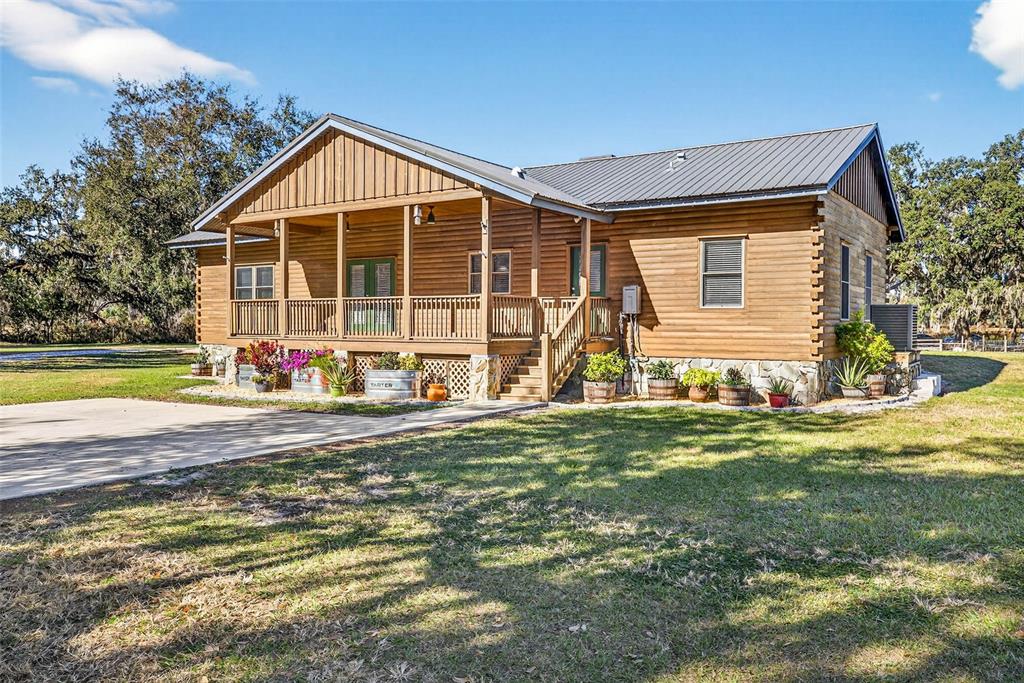 A wooden cabin with a metal roof and a covered front porch sits on grass — 6750 SUTTON OAKS LANE, ZEPHYRHILLS, FL