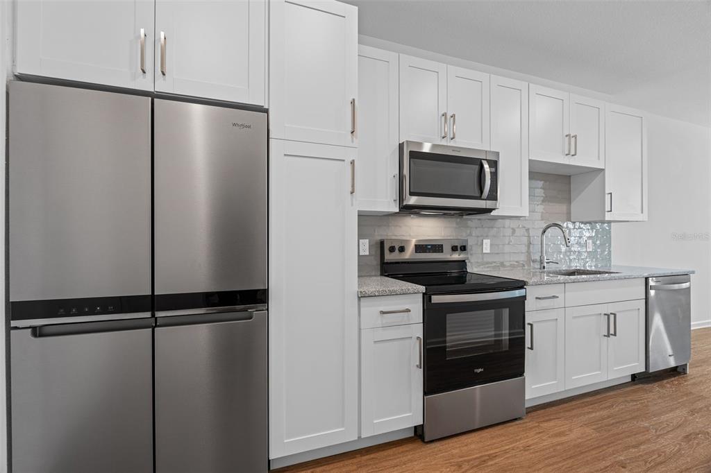 A modern kitchen features white shaker cabinets, stainless steel appliances, and light-colored granite countertops — 1700 RANCH ROAD UNIT A1-7305, NOKOMIS, FL