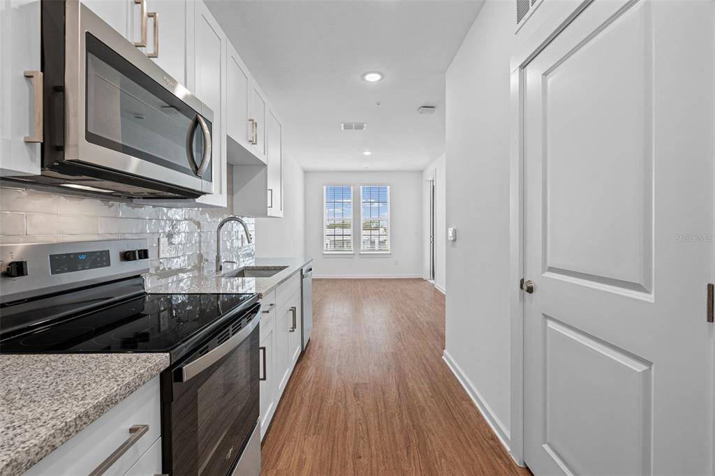 A modern kitchen features white cabinets, stainless steel appliances, granite countertops, and wood-look flooring — 1700 RANCH ROAD UNIT A1-7305, NOKOMIS, FL