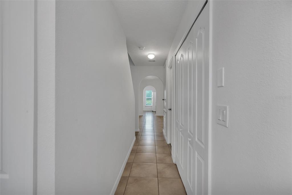 A hallway with tiled floors leads toward an arched doorway with a window beyond — 2900 CLARABELLE COURT, KISSIMMEE, FL