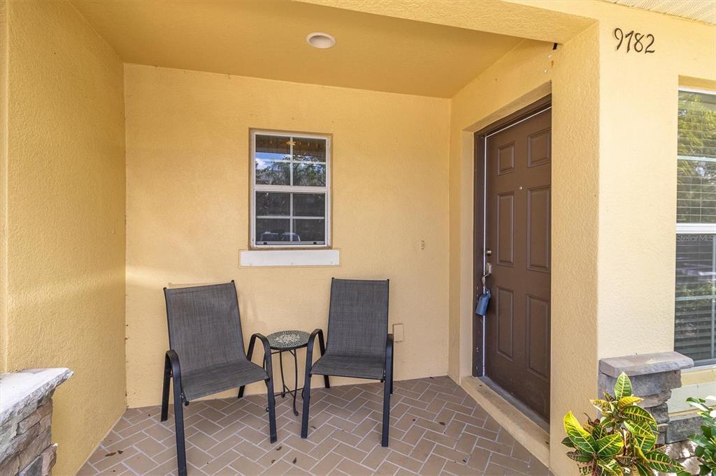 A covered front porch features a brick-patterned floor, two chairs, a small table, and a door — 9782 TRUMPET VINE LOOP, TRINITY, FL