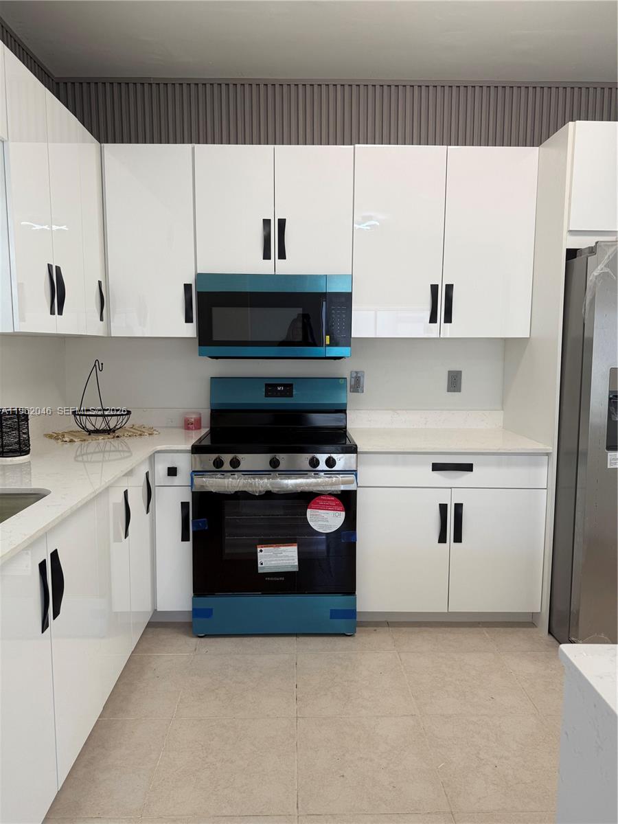 A kitchen features white cabinets, a stainless steel stove, a microwave, and light-colored countertops — 6793 SW 152nd Pl # 93, Miami FL 33193, MIAMI, FL