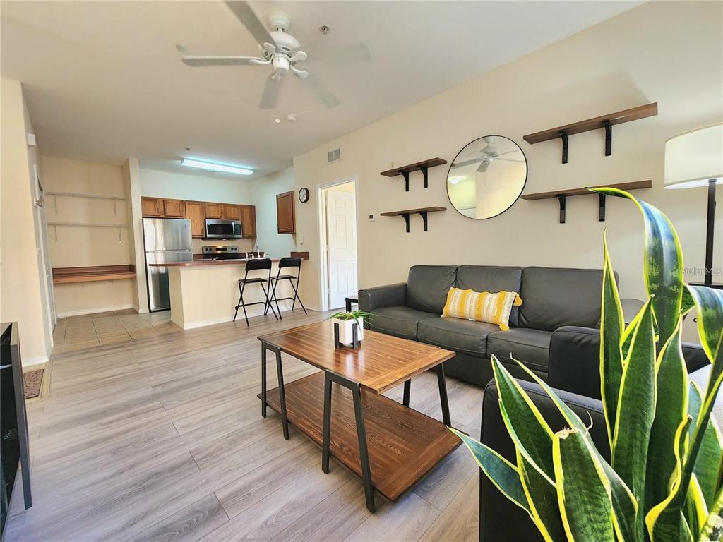 A living room with wood-look flooring, a grey sofa, and an open kitchen with bar seating — 8137 CLAIRE ANN DRIVE UNIT 203, ORLANDO, FL